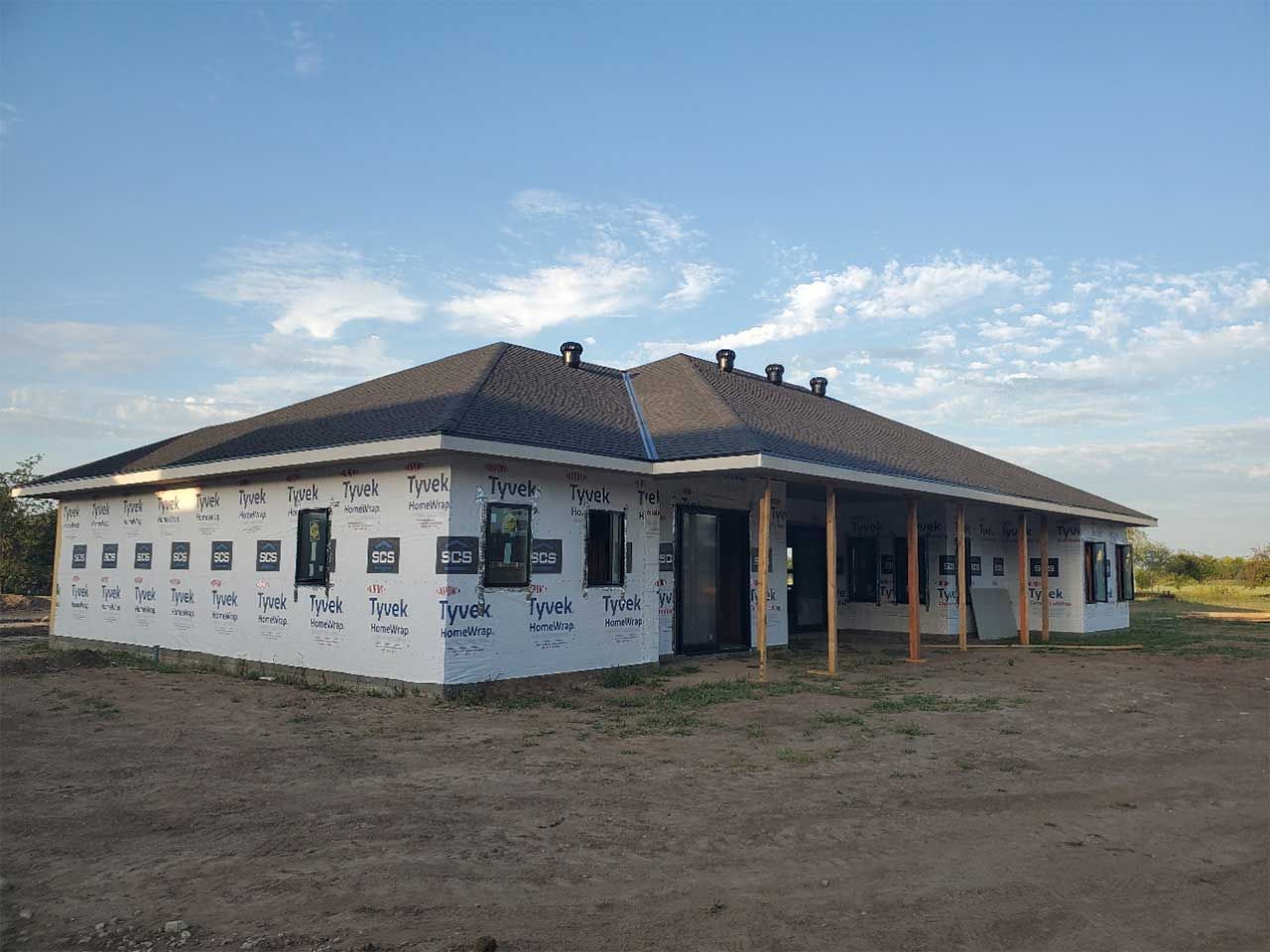 A large house is being built in the middle of a dirt field.