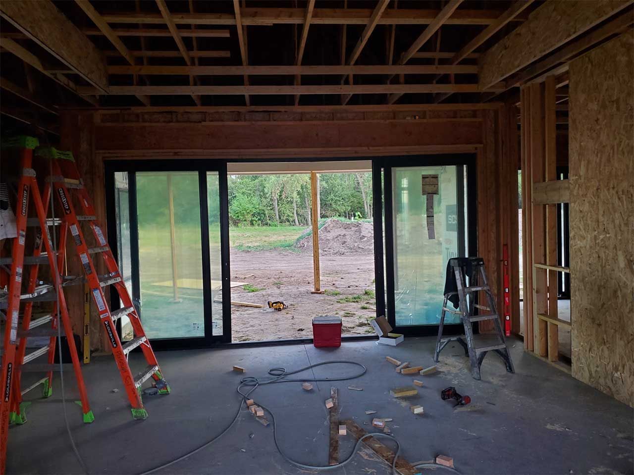 A room in a house under construction with sliding glass doors and ladders.