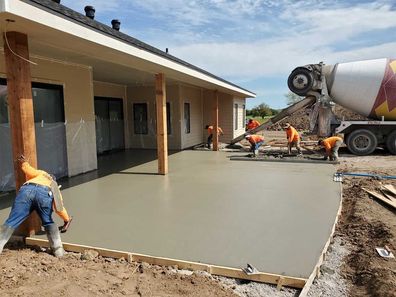 A group of construction workers are working on a concrete driveway in front of a house.