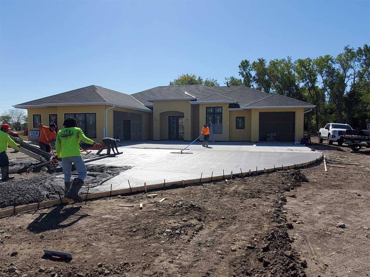 A group of people are working on a concrete driveway in front of a house.