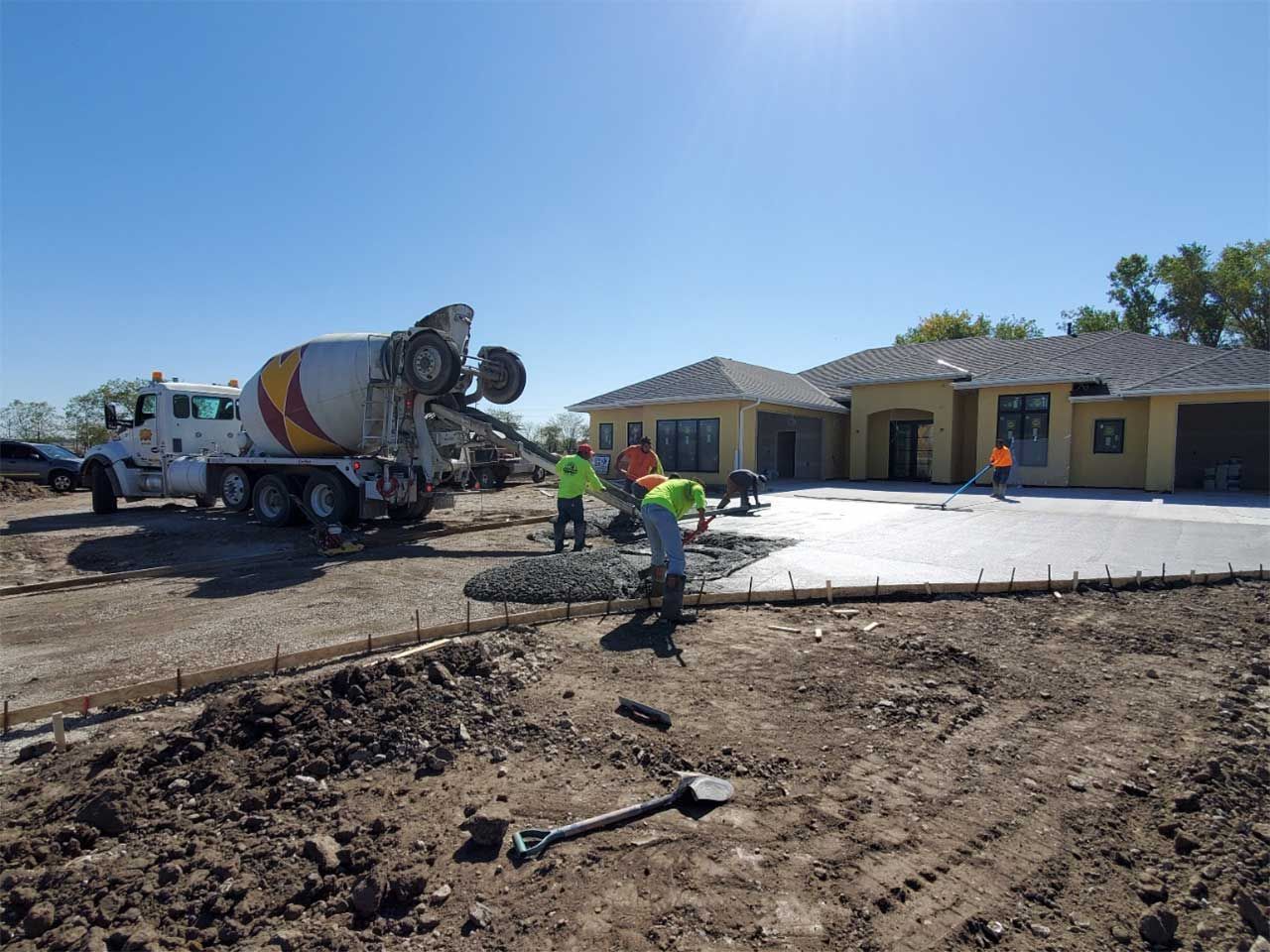 A concrete mixer truck is pouring concrete into a driveway in front of a house.