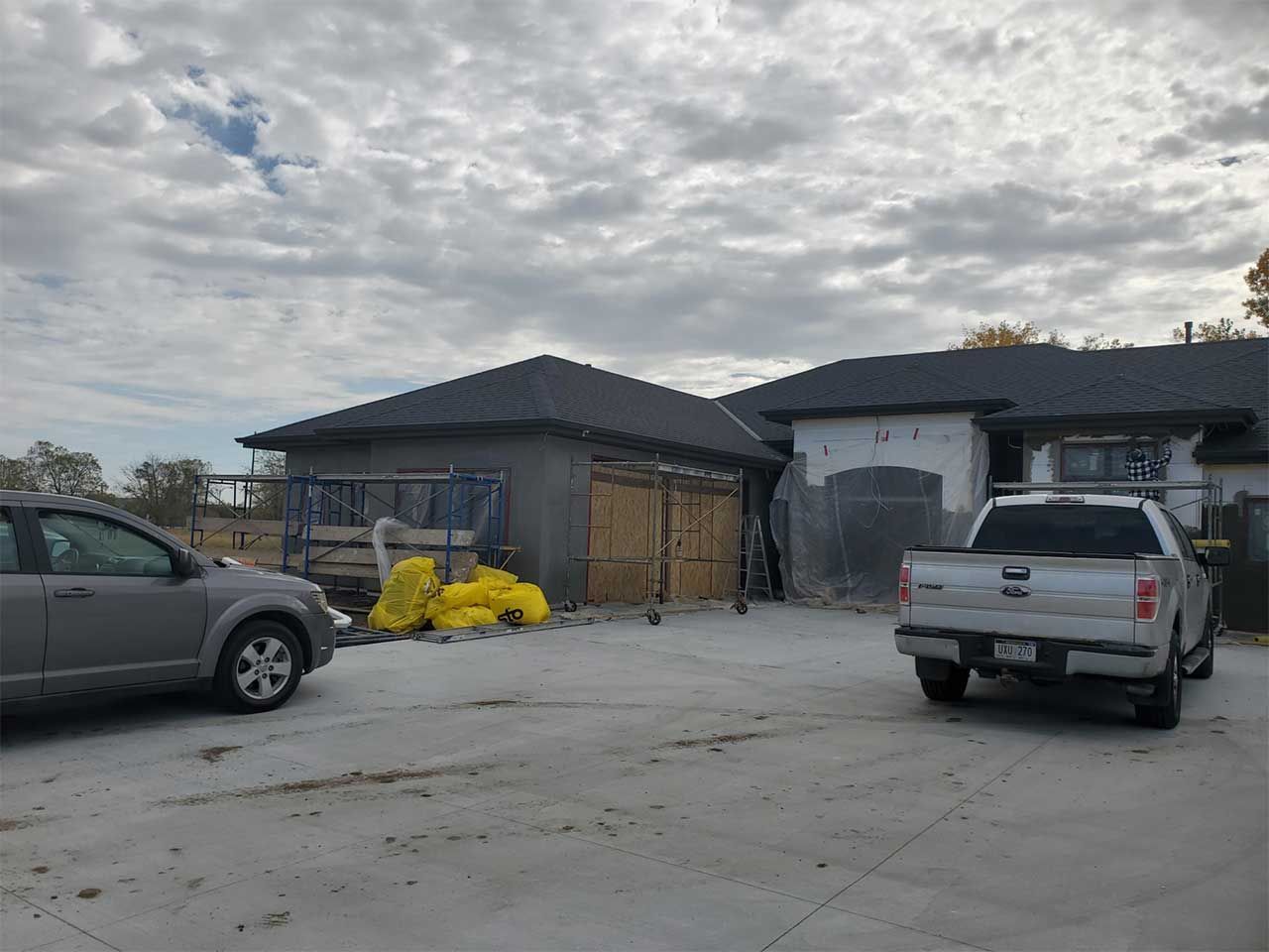 A car and a truck are parked in front of a house under construction.
