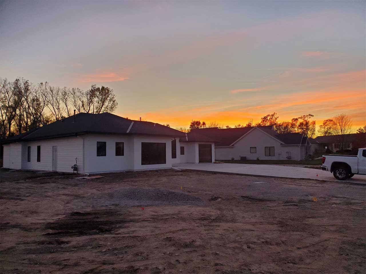 A white truck is parked in front of a house at sunset.