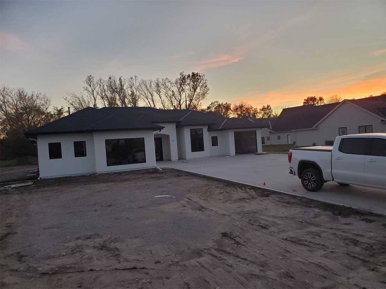 A white truck is parked in front of a house under construction.