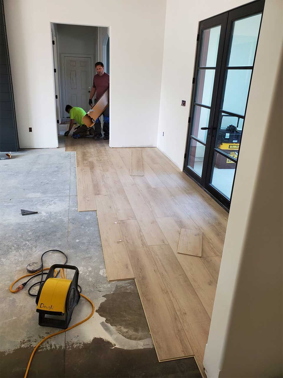 Two men are working on a wooden floor in a room.