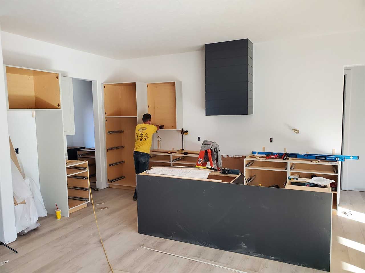 A man in a yellow shirt is working on a kitchen.
