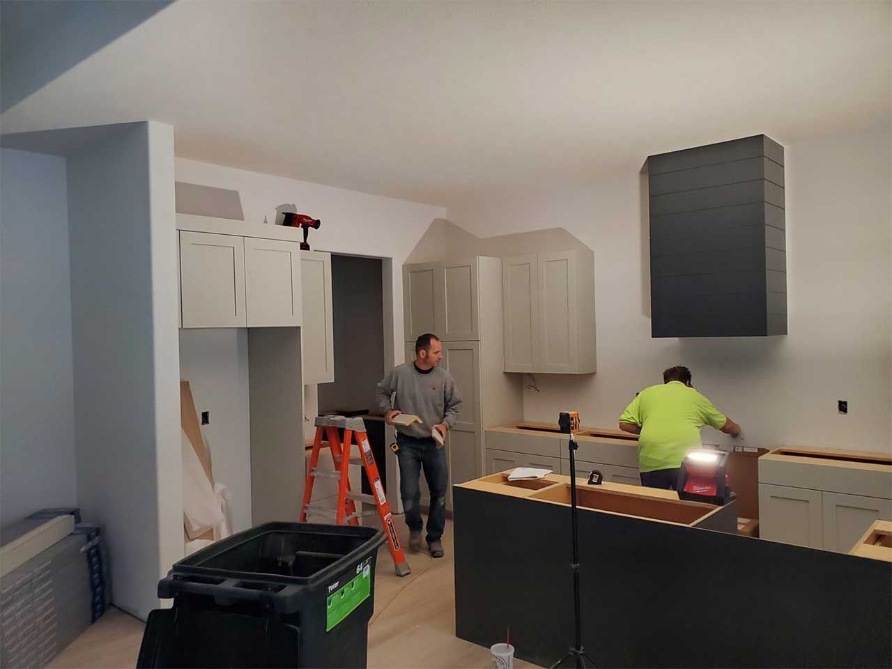 Two men are working in a kitchen with a trash can in the foreground.