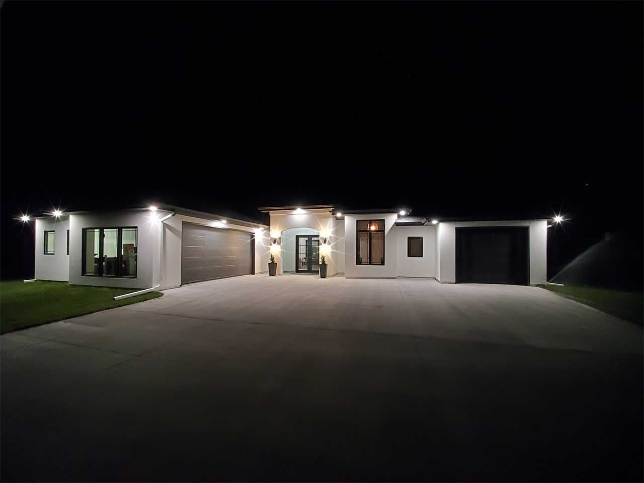 A large white house is lit up at night with a driveway leading to it.