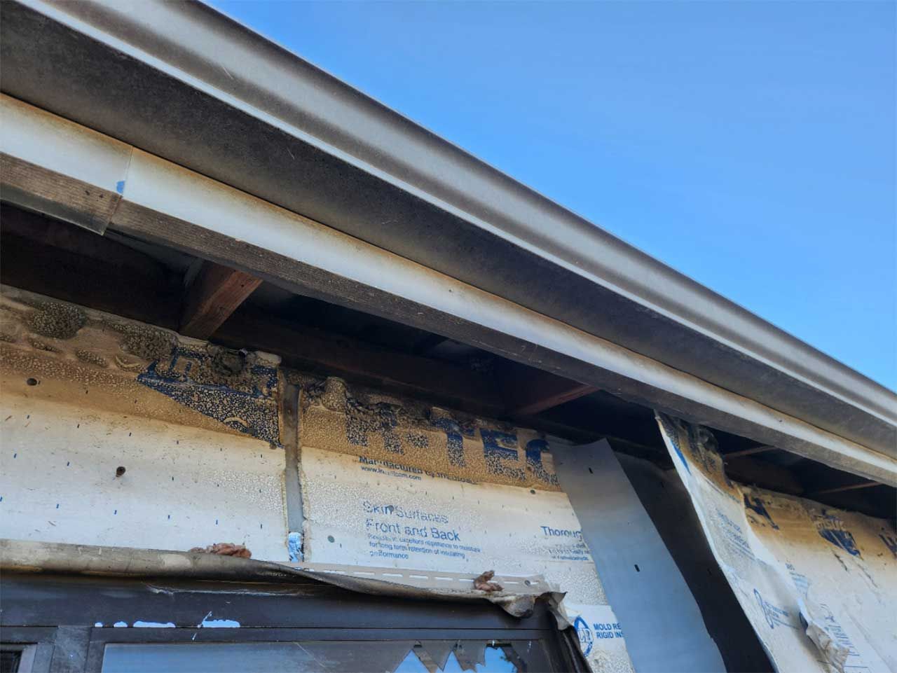 A roof with a gutter and a window with a blue sky in the background