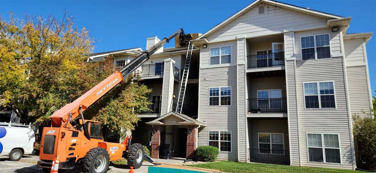 A man is working on the roof of a large apartment building.