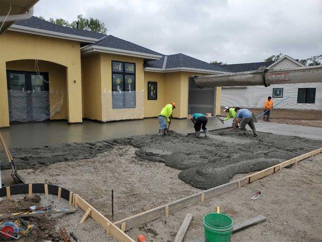 A group of construction workers are working on a concrete driveway in front of a house.