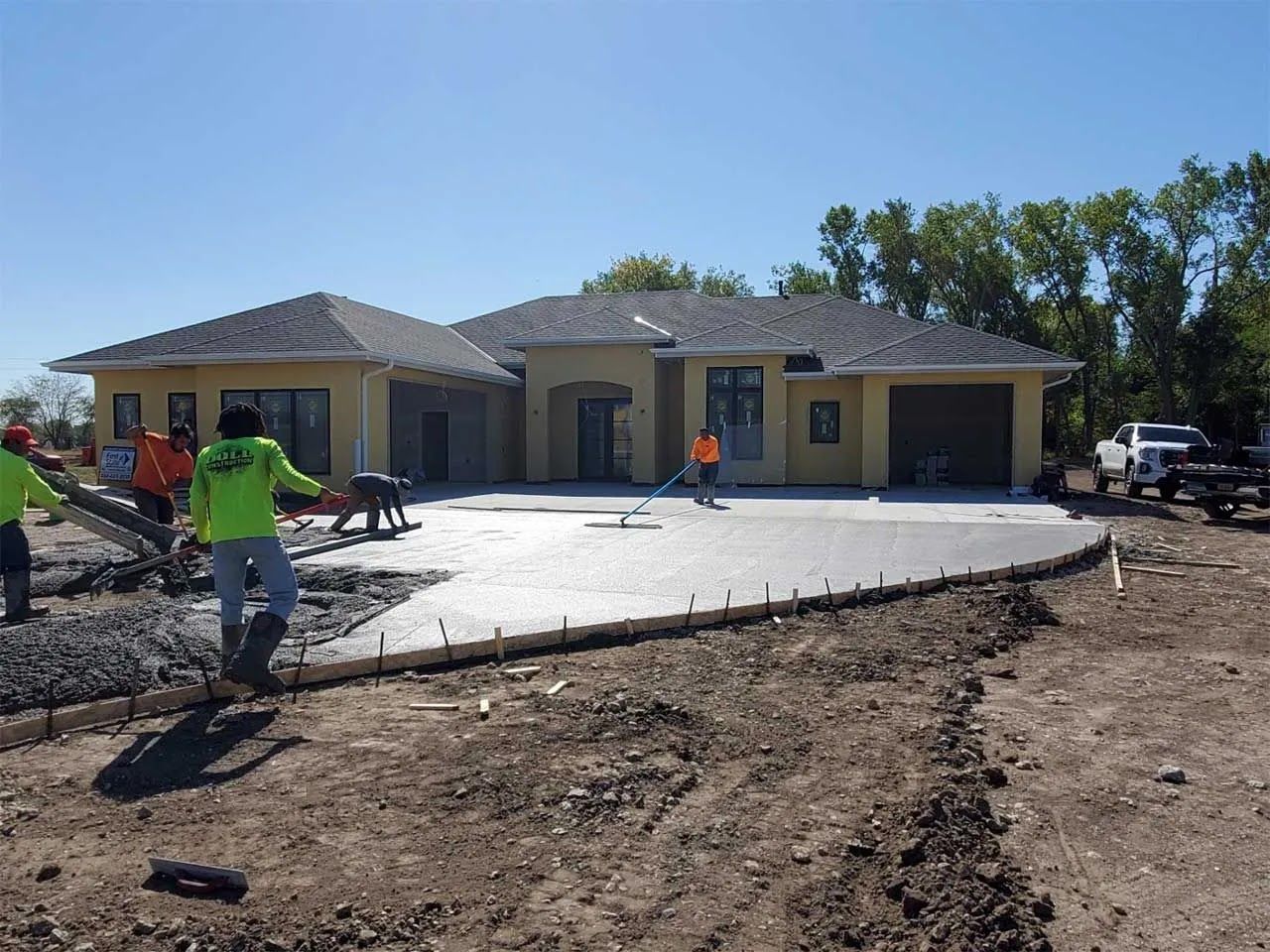 A group of construction workers are working on a driveway in front of a house.