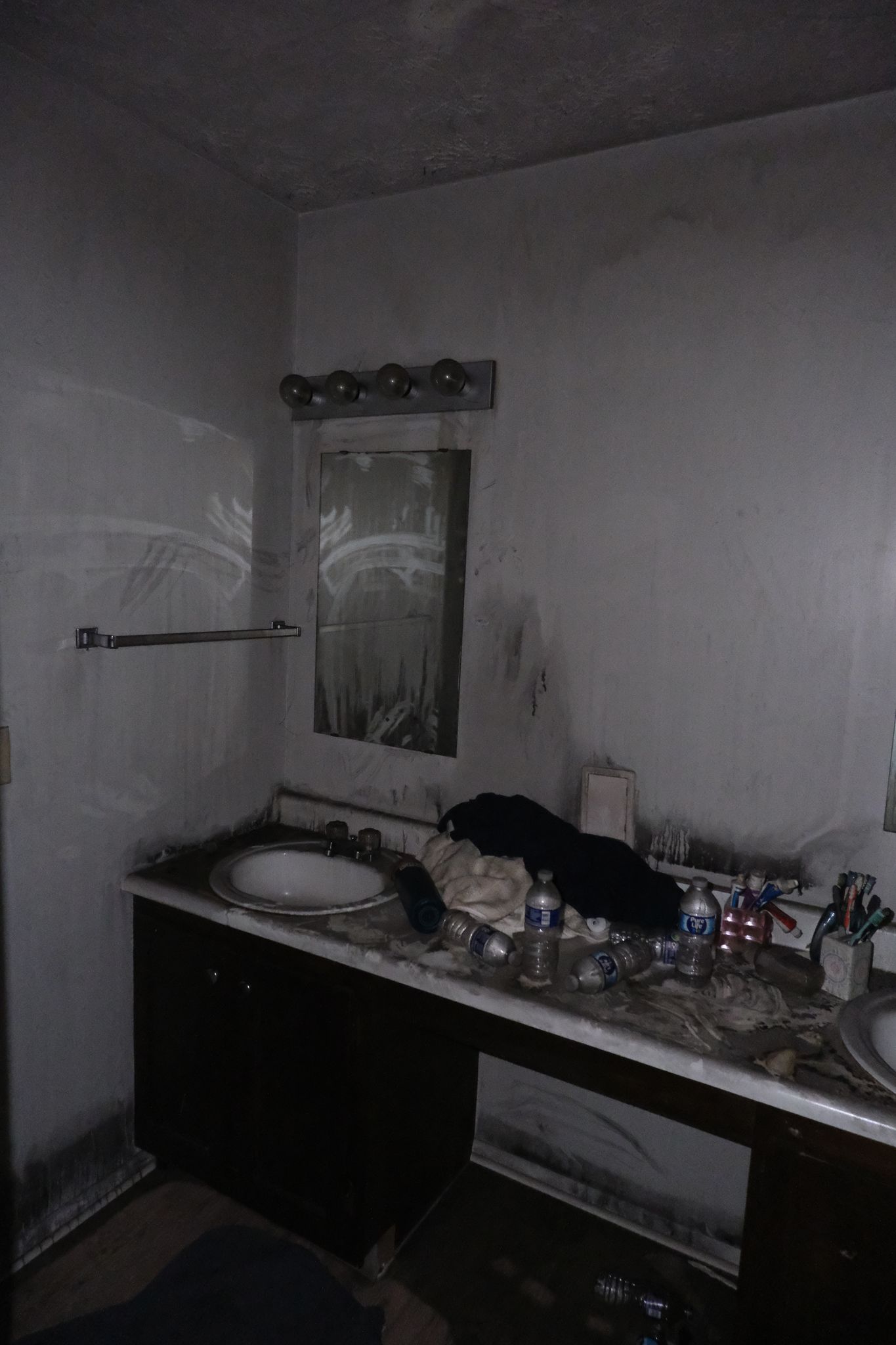 Bathroom with soot-covered walls and vanity. Debris on counter, mirror visible.