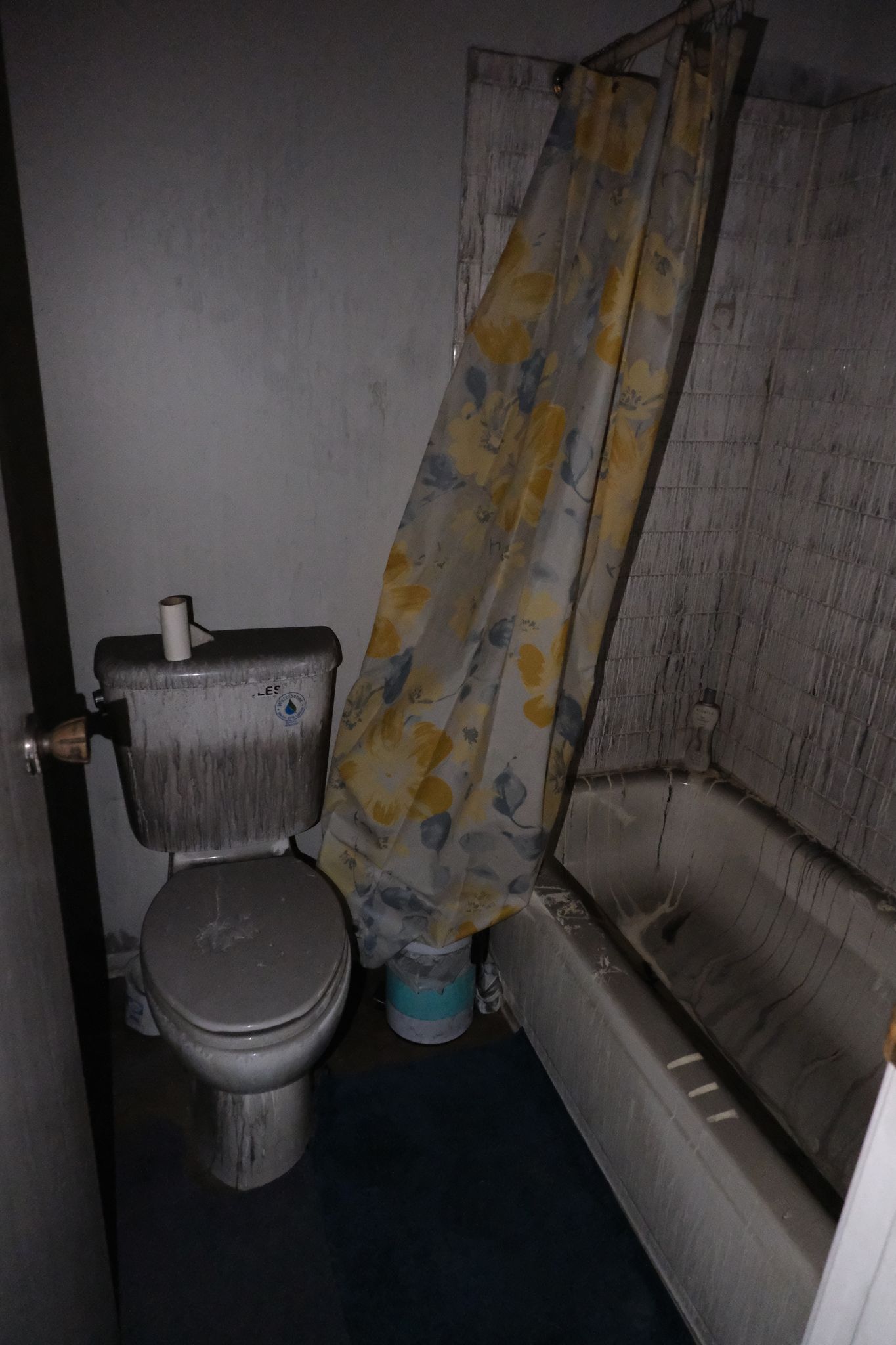 Dusty, dirty bathroom with toilet, tub, and shower curtain. Poor condition.