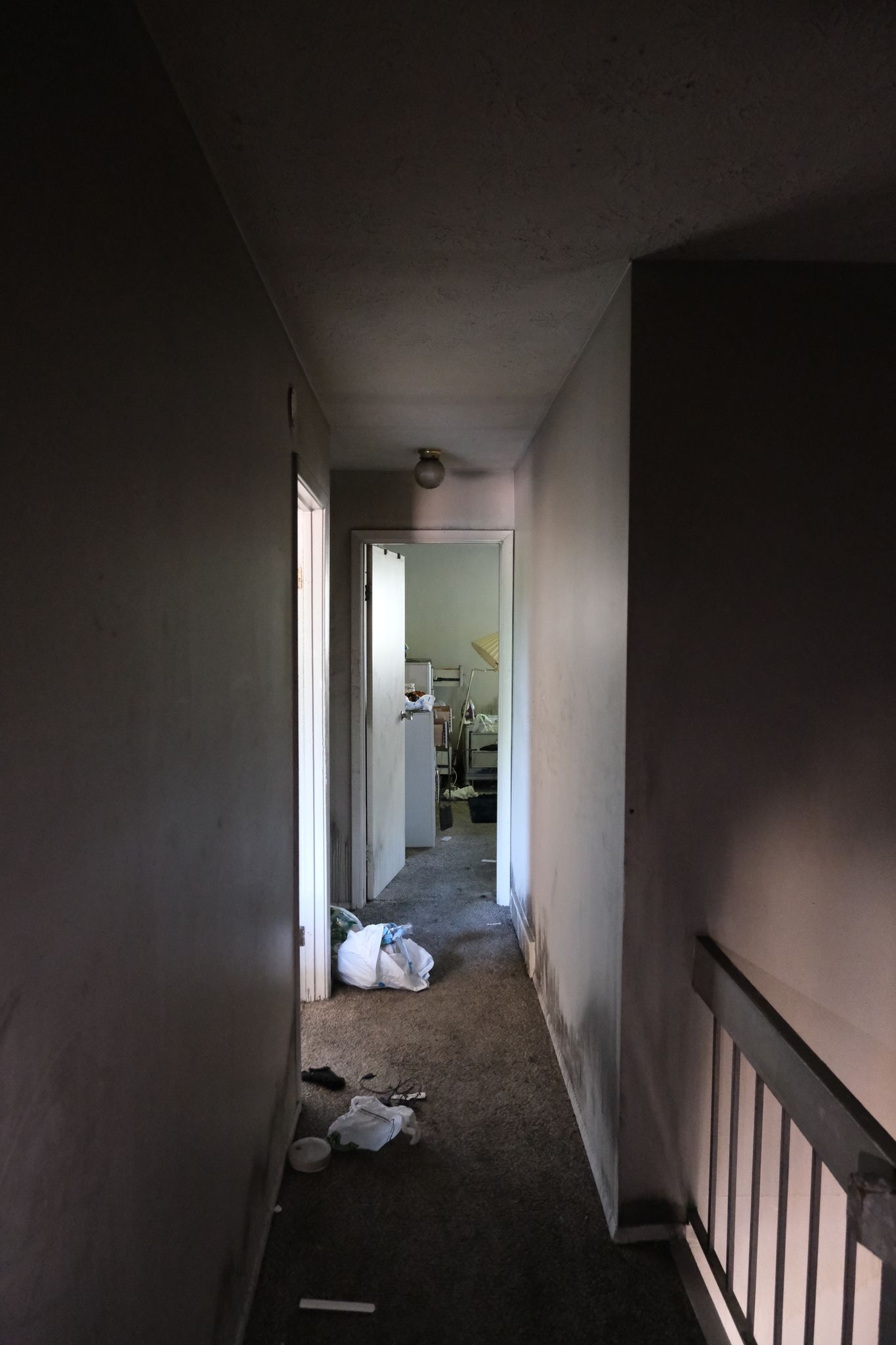 Narrow, dimly lit hallway with doors, debris on the floor, and a railing.