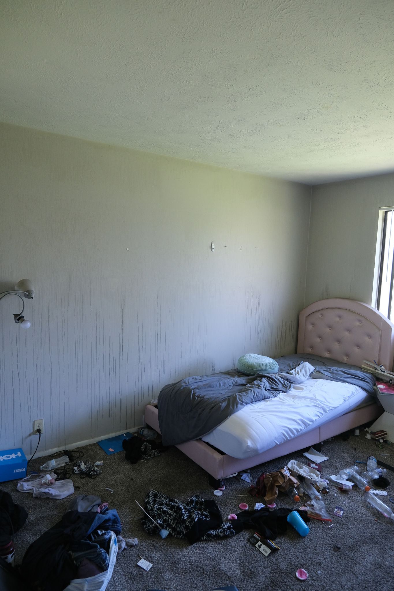 Cluttered bedroom with a pink bed, dirty walls, and trash on the floor.