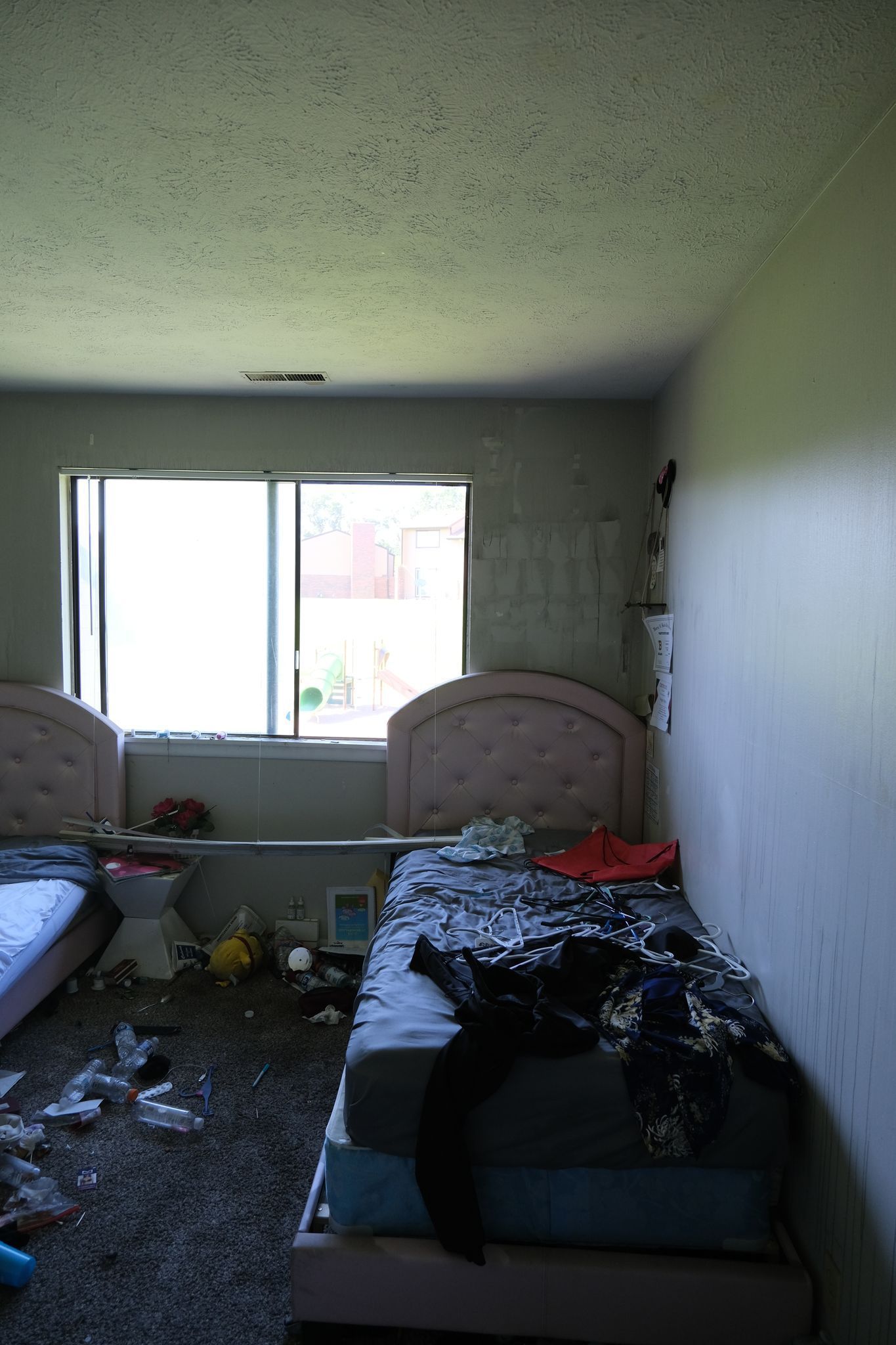 Messy bedroom with two beds, a window, and trash on the floor.