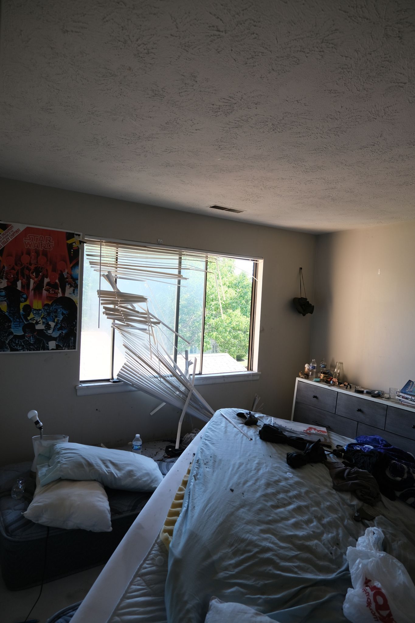 Messy bedroom with a window, bed, and artwork. Light from the window illuminates the room.