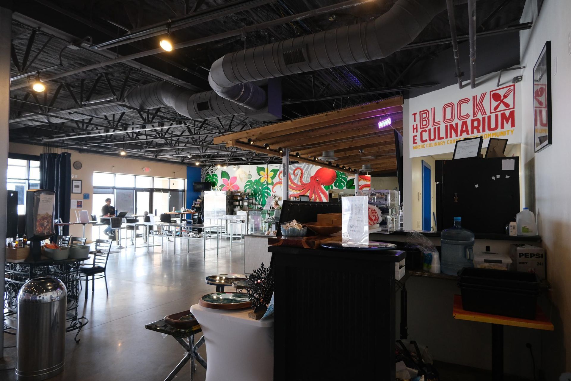 Spacious interior of The Block Culinarium, featuring exposed industrial ceiling, concrete floors, and a mural.