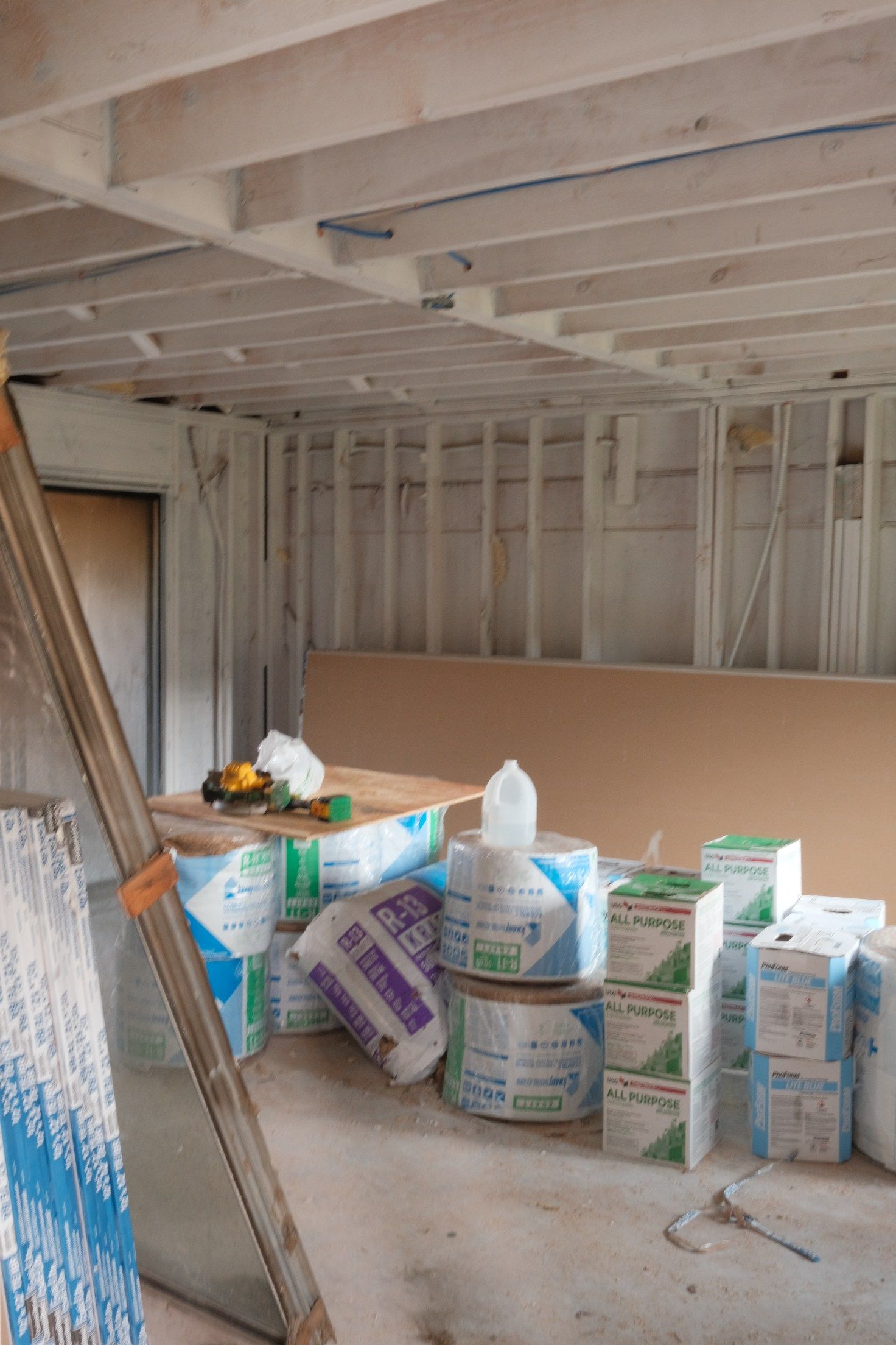 Interior of a room under construction with insulation, drywall, and tools scattered about.
