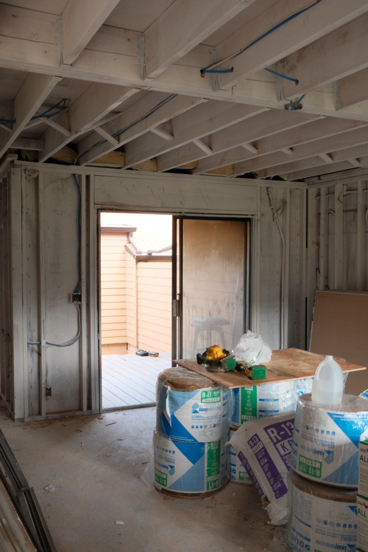 Interior of a room under construction with open sliding door to outside deck. Materials and tools scattered.