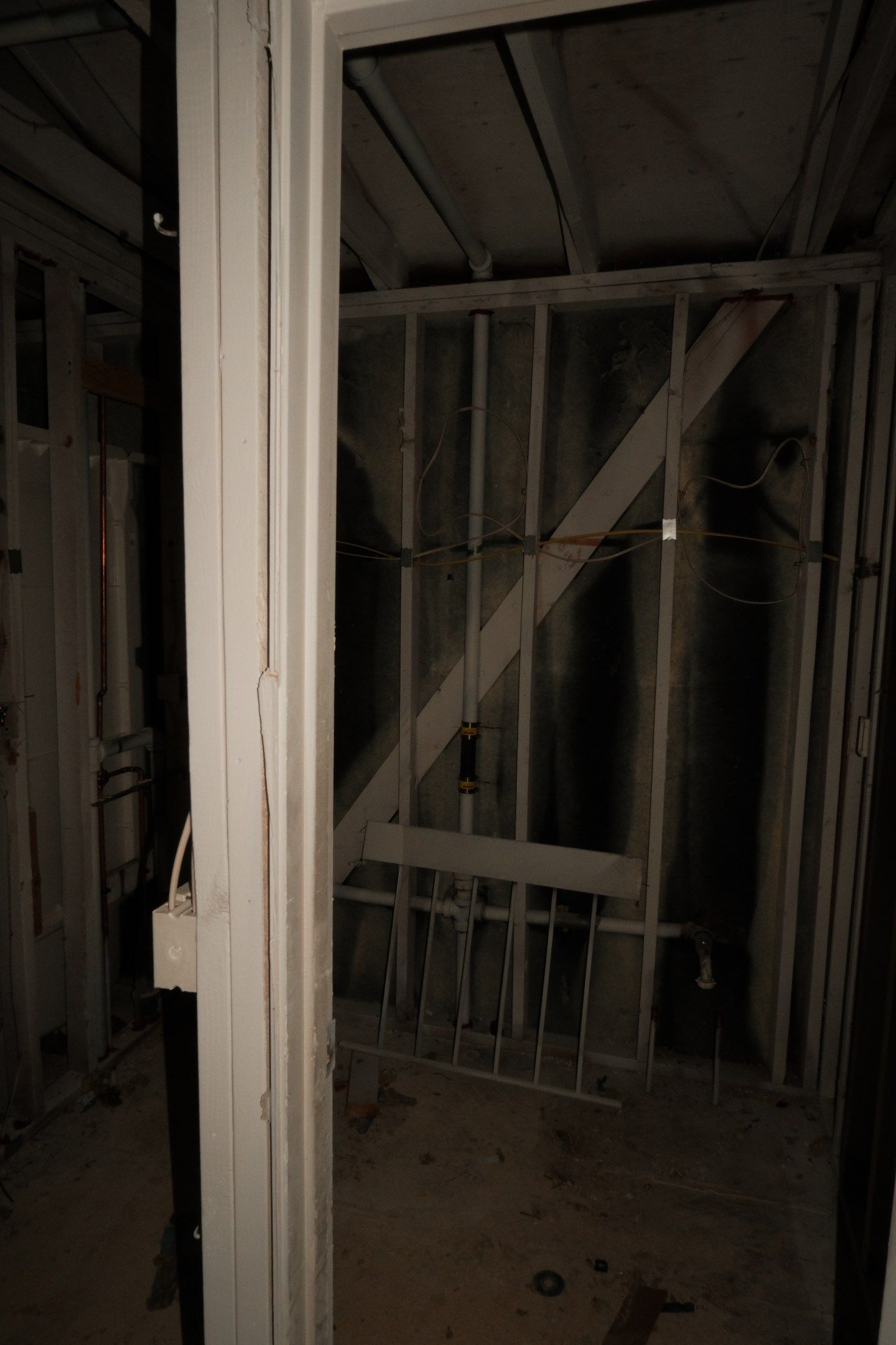View through a doorway into a dark, unfinished room with wooden framing and metal bars.