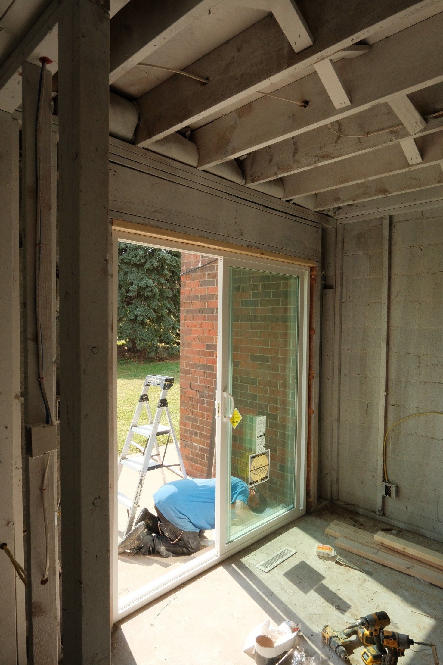 Construction site with sliding glass door, person working outside, exposed beams, concrete walls.