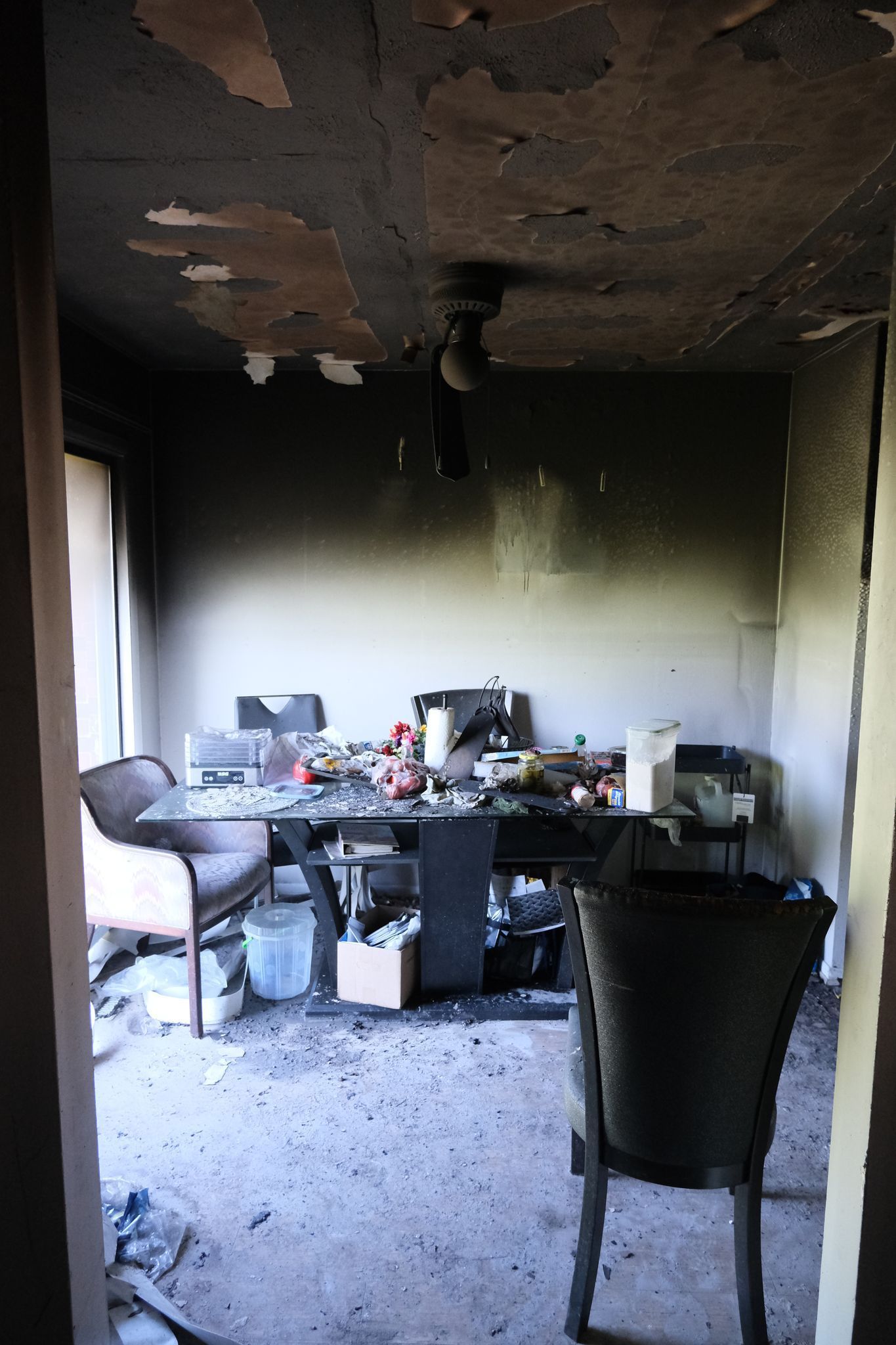 Fire-damaged room: charred walls and ceiling, debris on a table, two chairs.