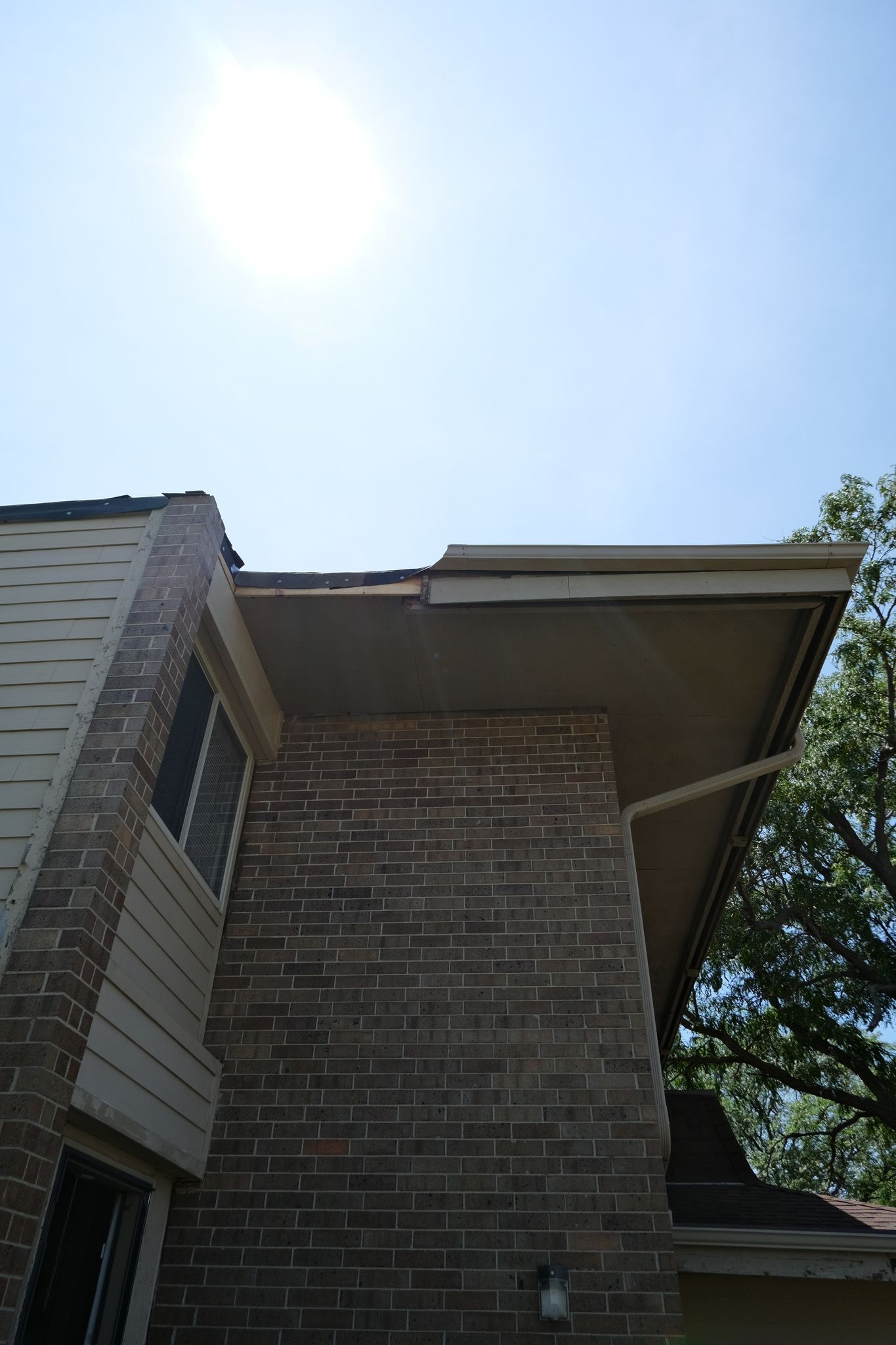 A two-story brick house with a flat roof and a bright sun in the sky.