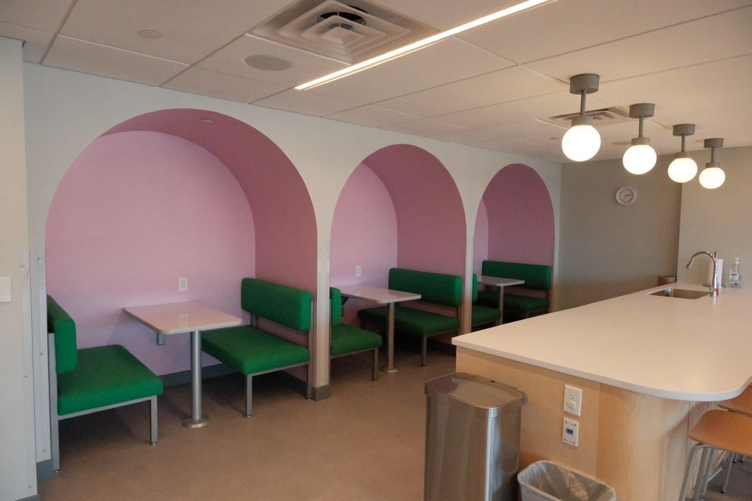 A room with pink arches and green benches and tables