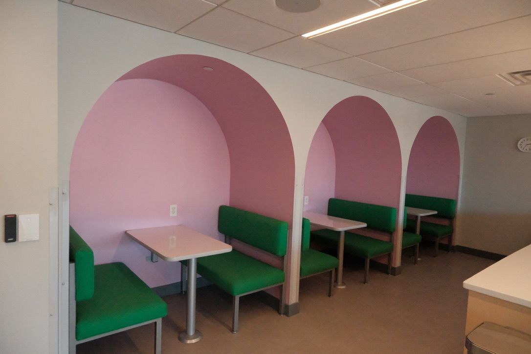 A room with pink arches and green benches and tables