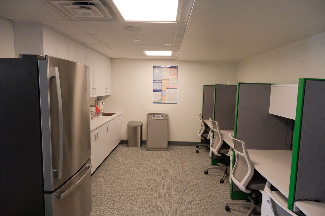 A kitchen with a refrigerator , sink , chairs and cubicles.
