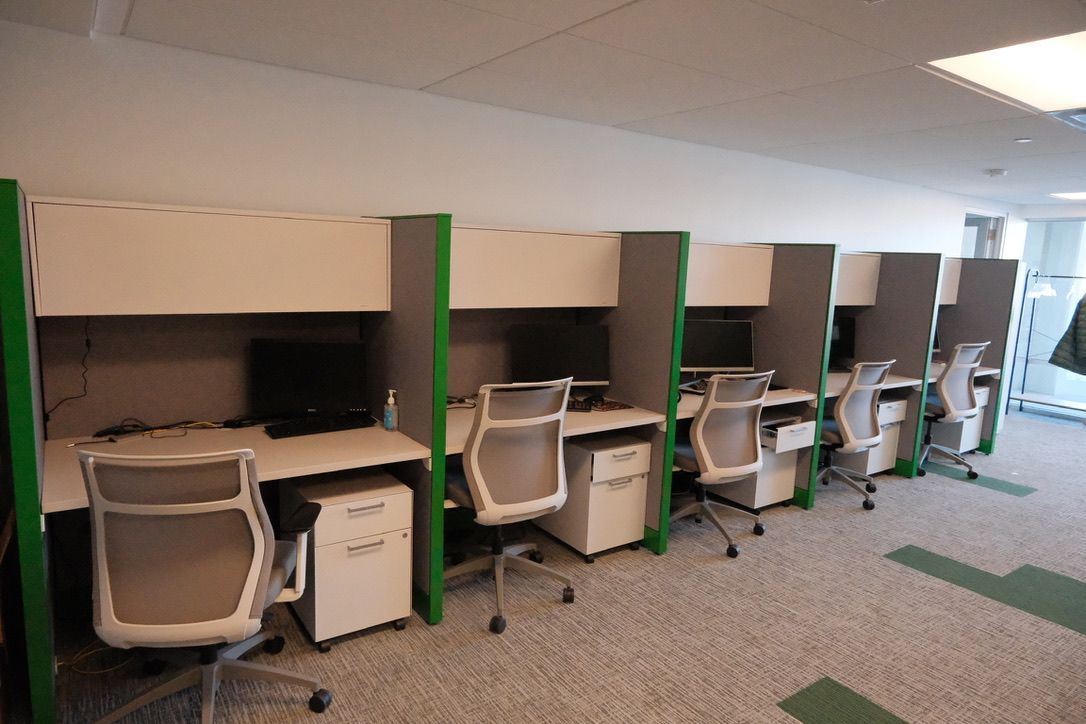 A row of cubicles with computers and chairs in an office.