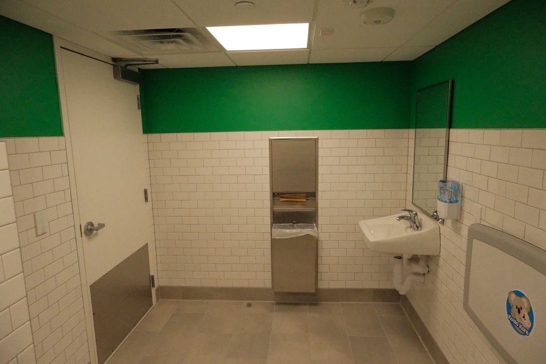 A bathroom with white tiles and green walls has a sink and a changing table.