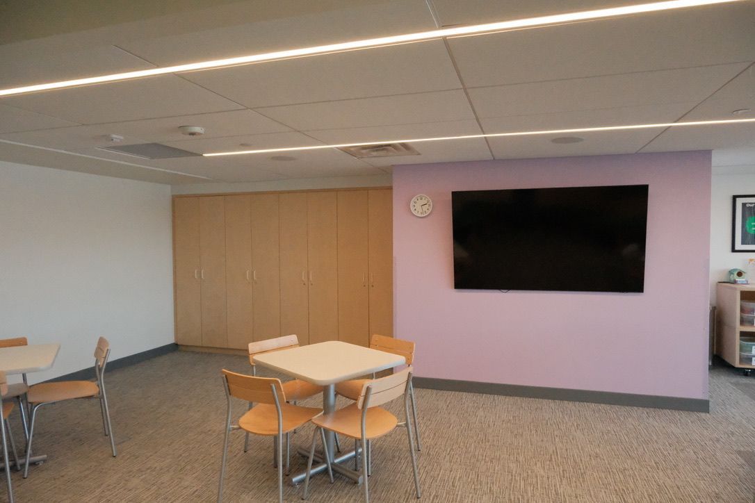 A room with tables and chairs and a flat screen tv on the wall.
