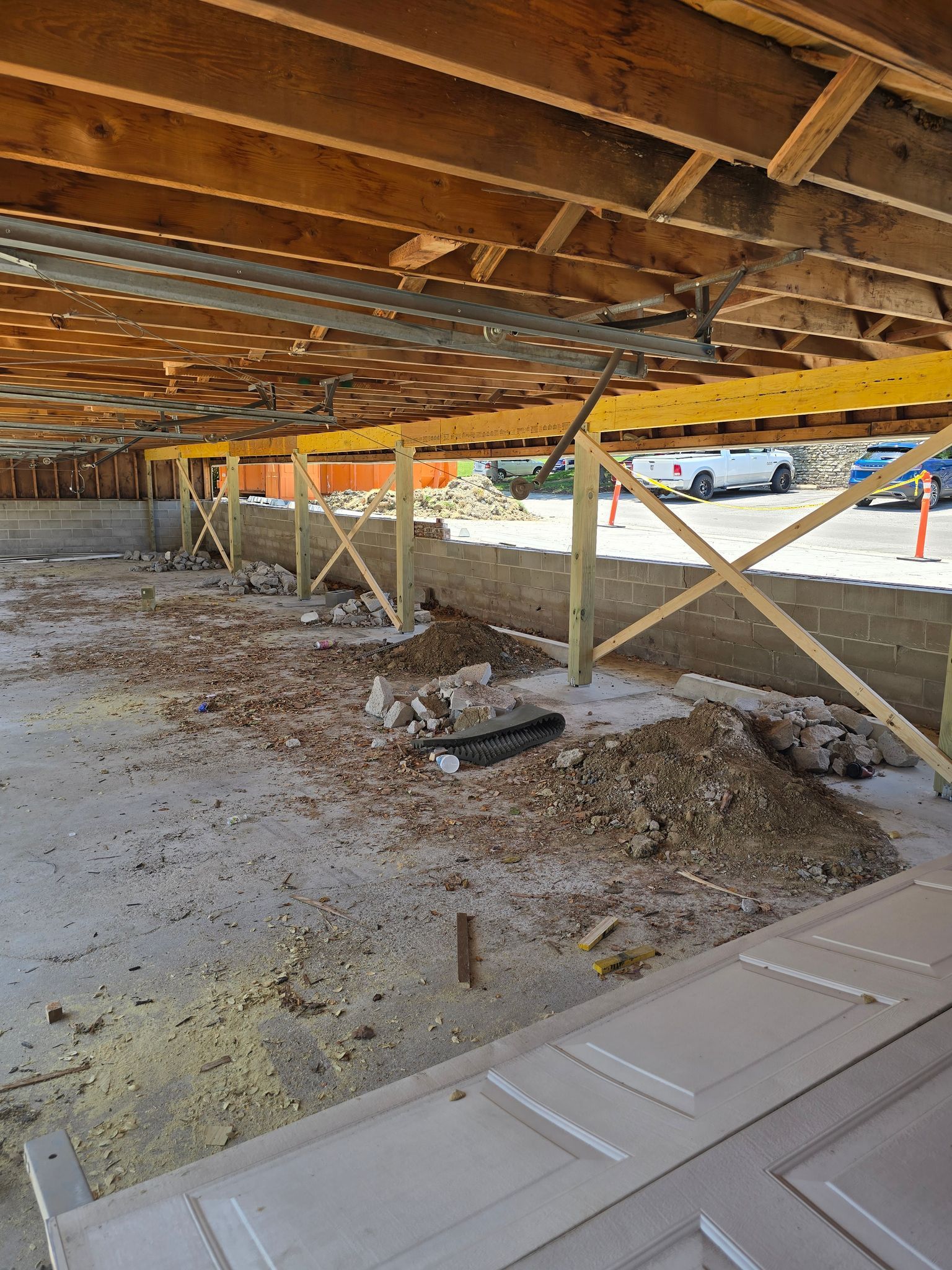 Underneath a building, wooden supports hold up the ceiling during construction; debris covers the concrete floor.