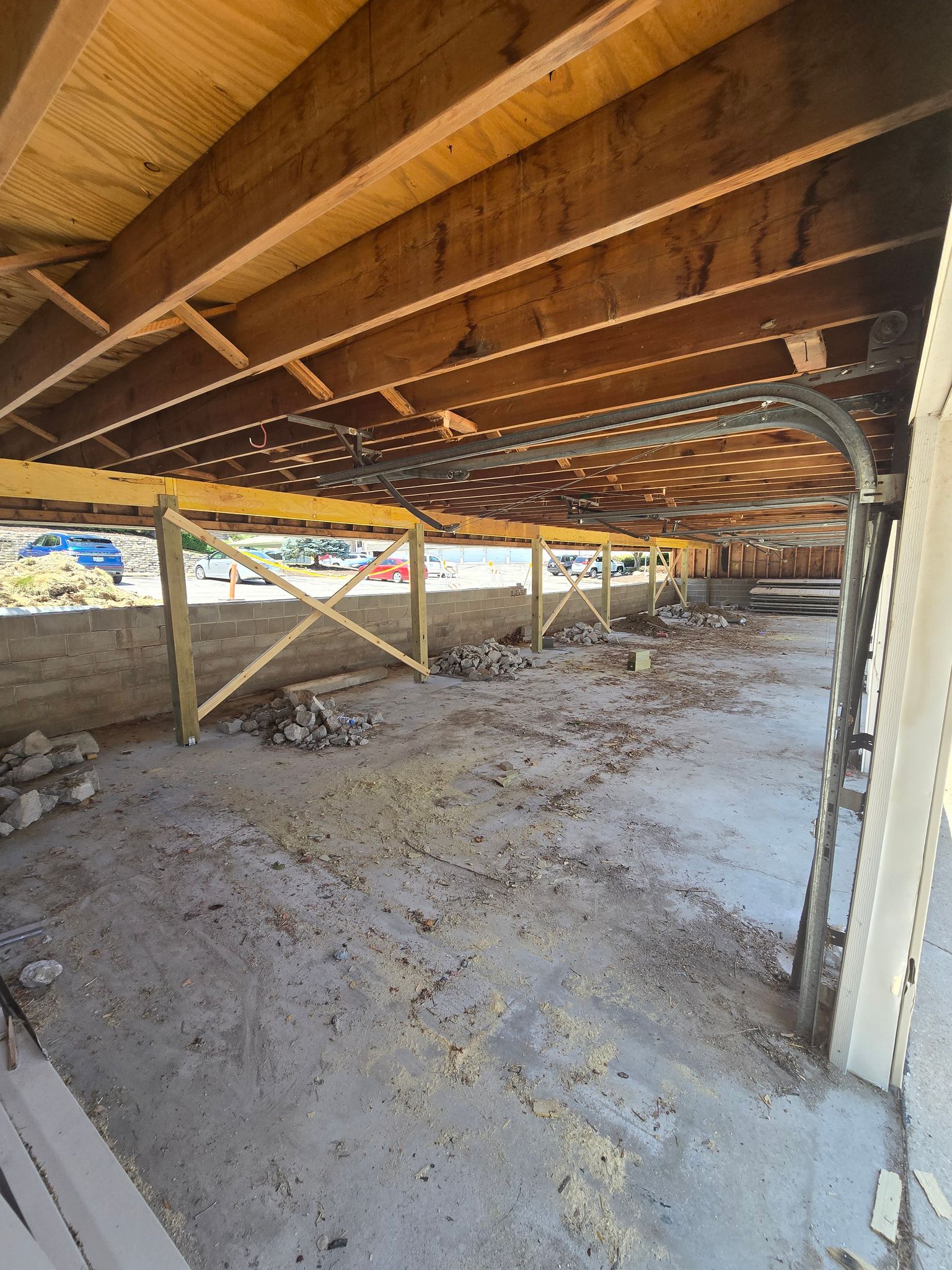 Under-construction structure with wooden beams, cement floor, and a garage door frame.