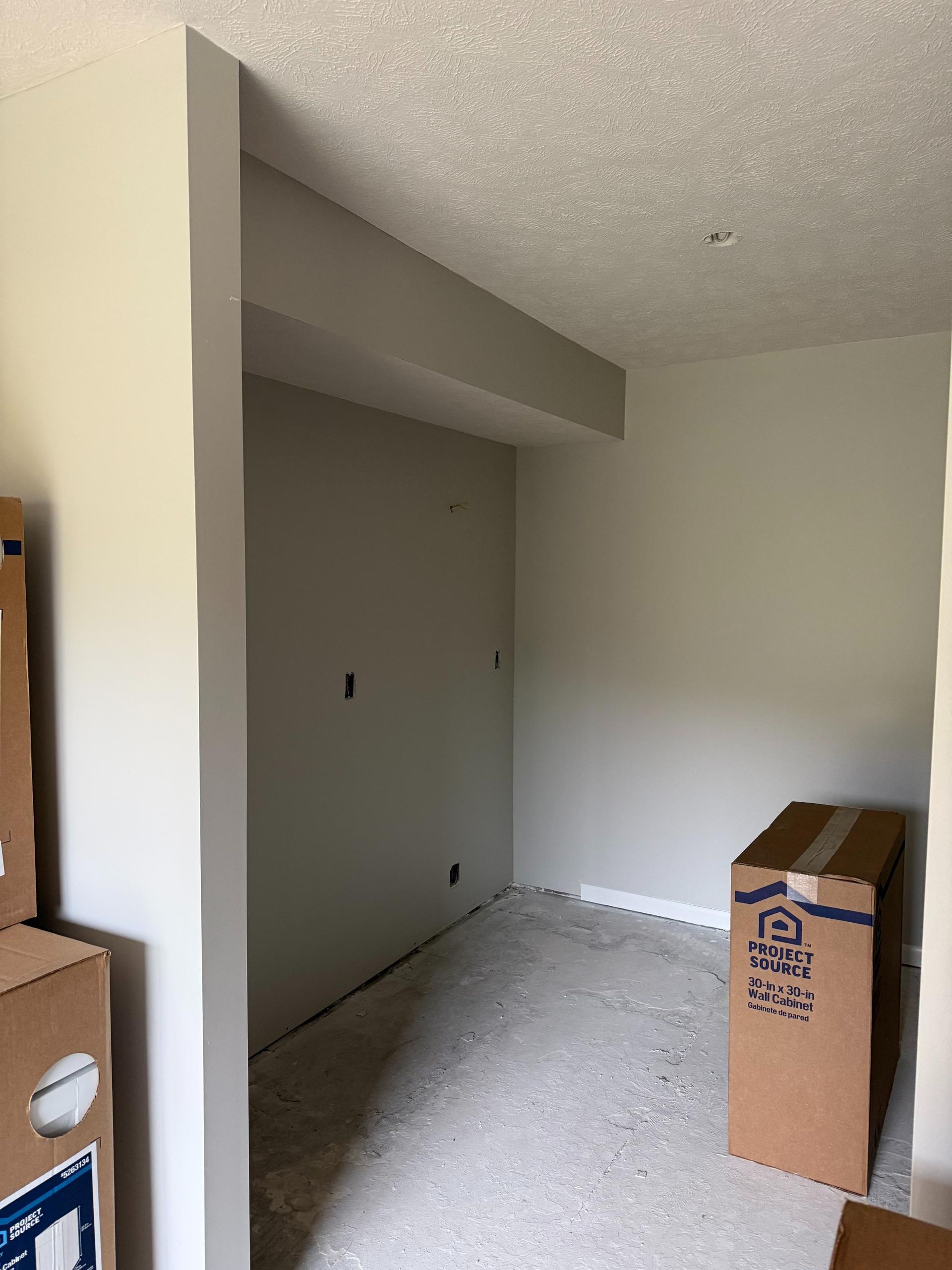 Empty room with gray walls and a support beam. Cardboard boxes on the floor.