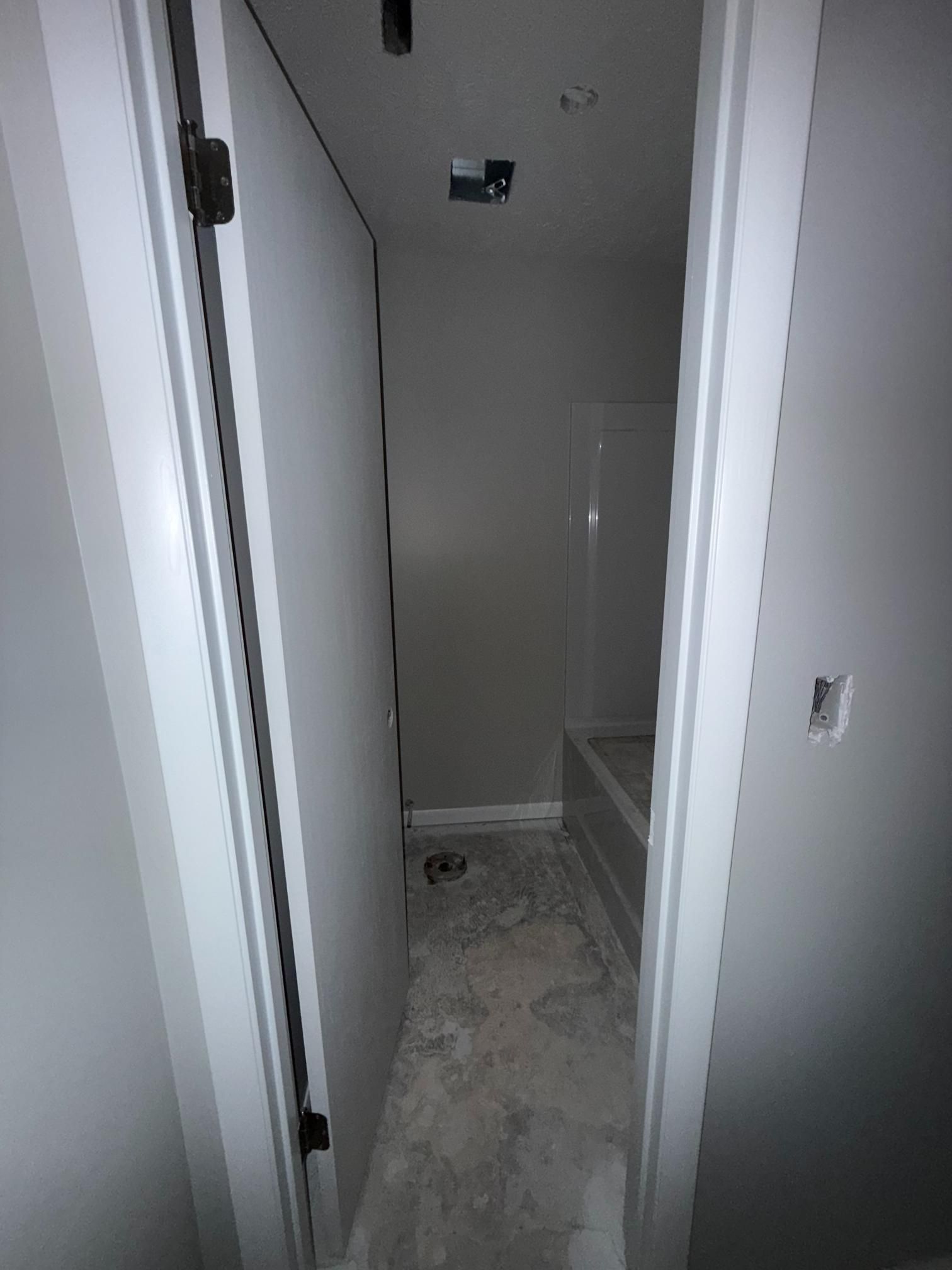 Narrow bathroom with a bathtub, unfinished concrete floor, and a closed door.