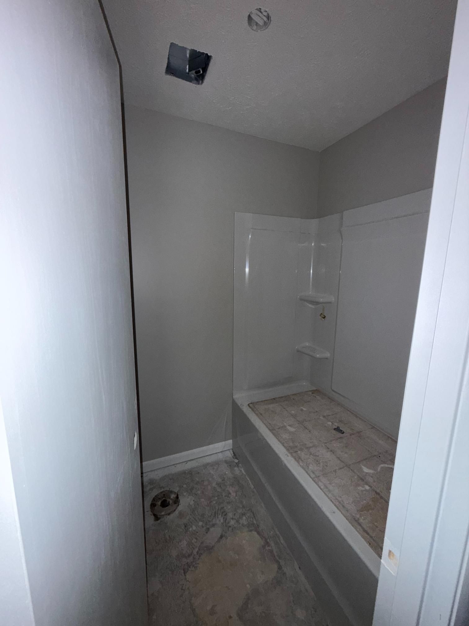 Small, unfinished bathroom with gray walls, white tub, and exposed floor.