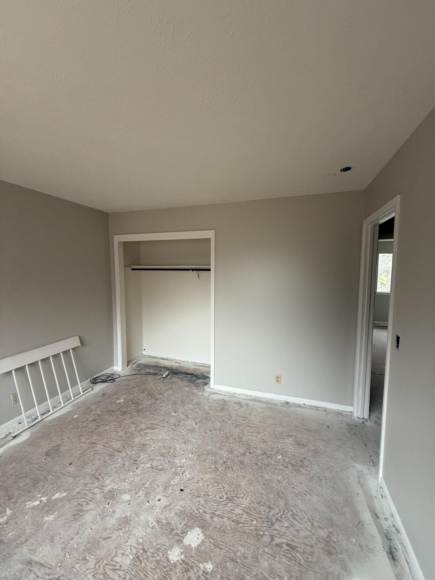 Empty room with grey walls, white trim, closet, and floor in need of finishing.