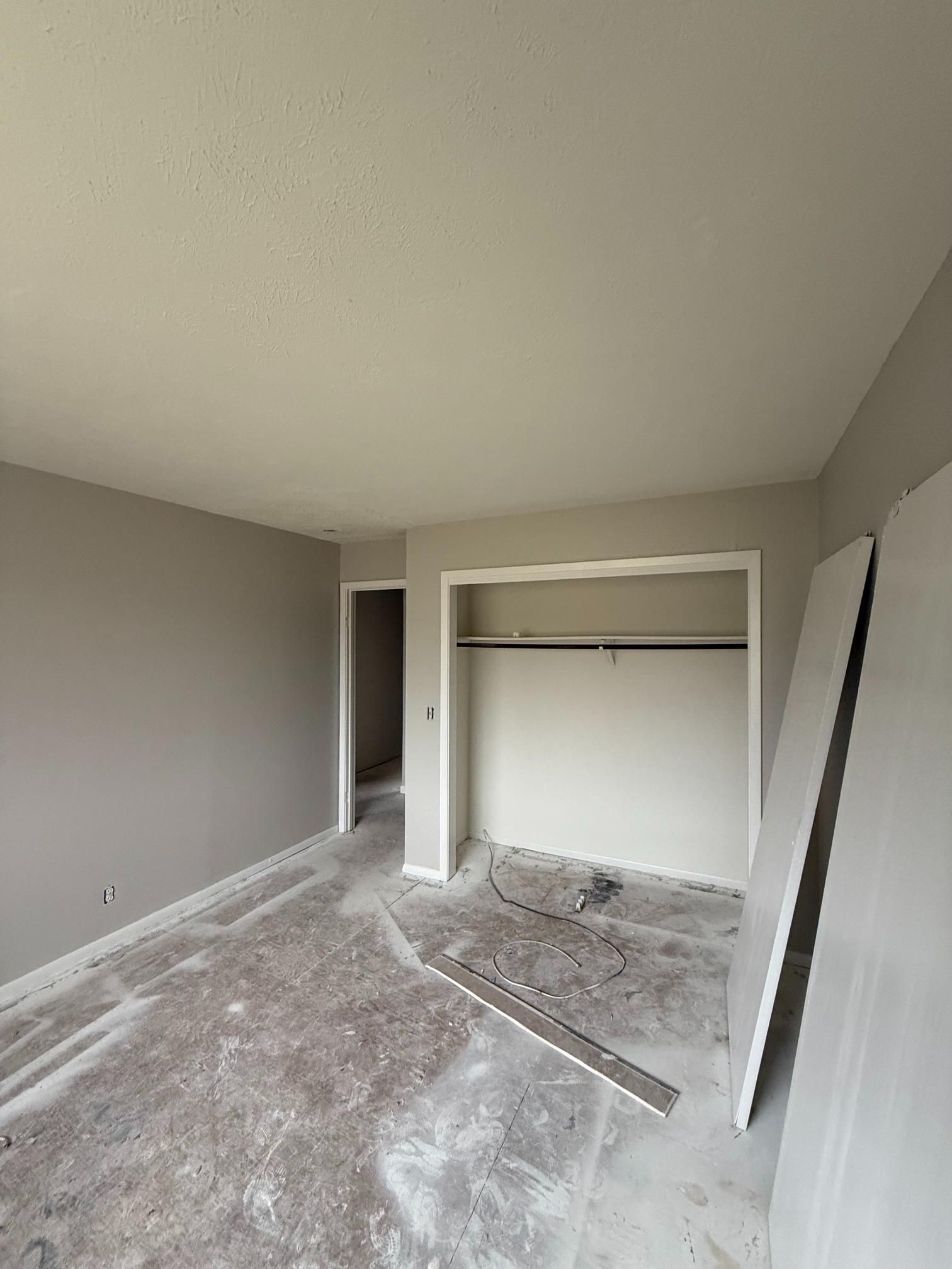 Empty room under construction with gray walls, white closet, and exposed flooring.