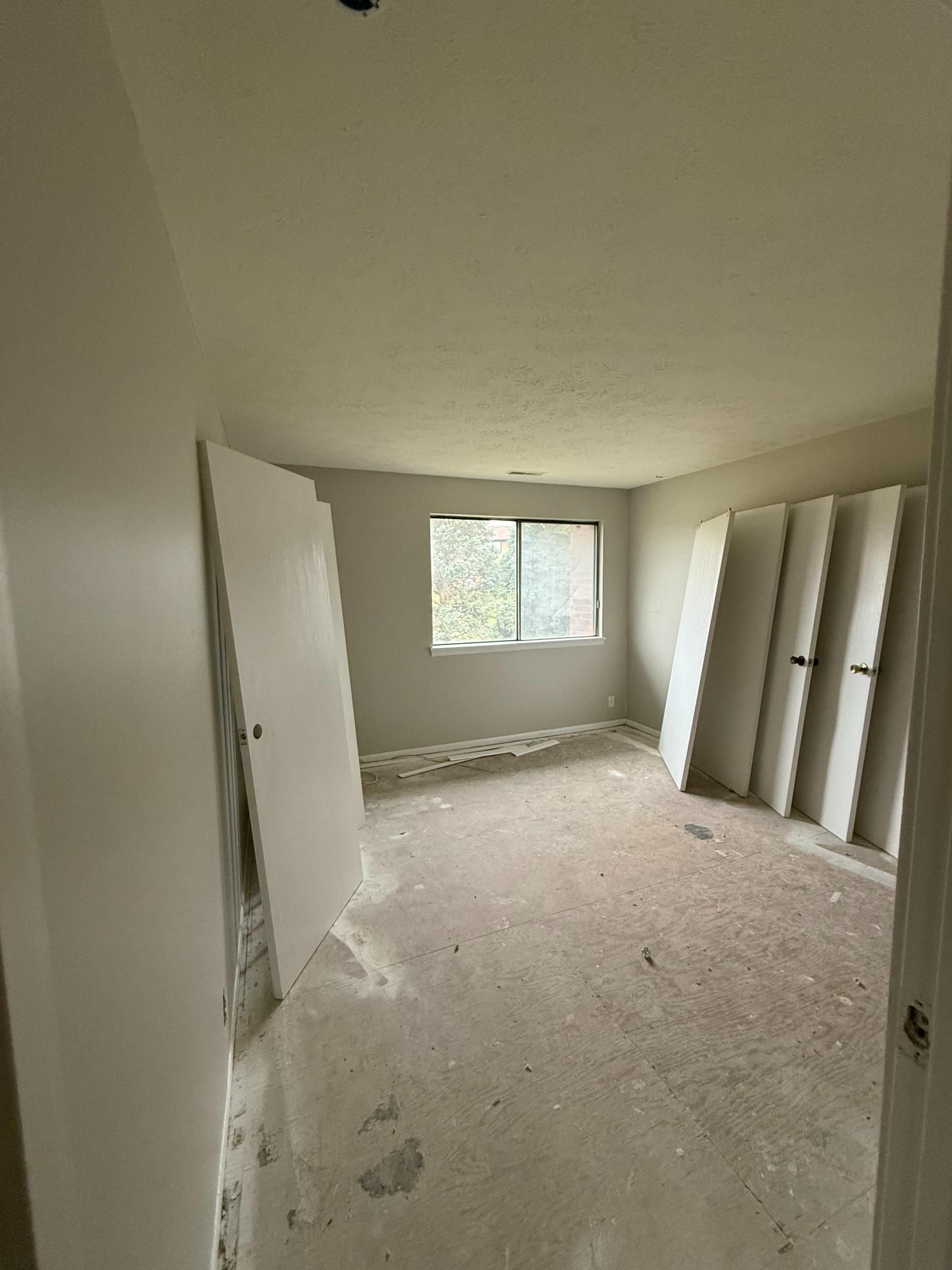 A bare room with white walls and a window. Several white doors are leaning against a wall.