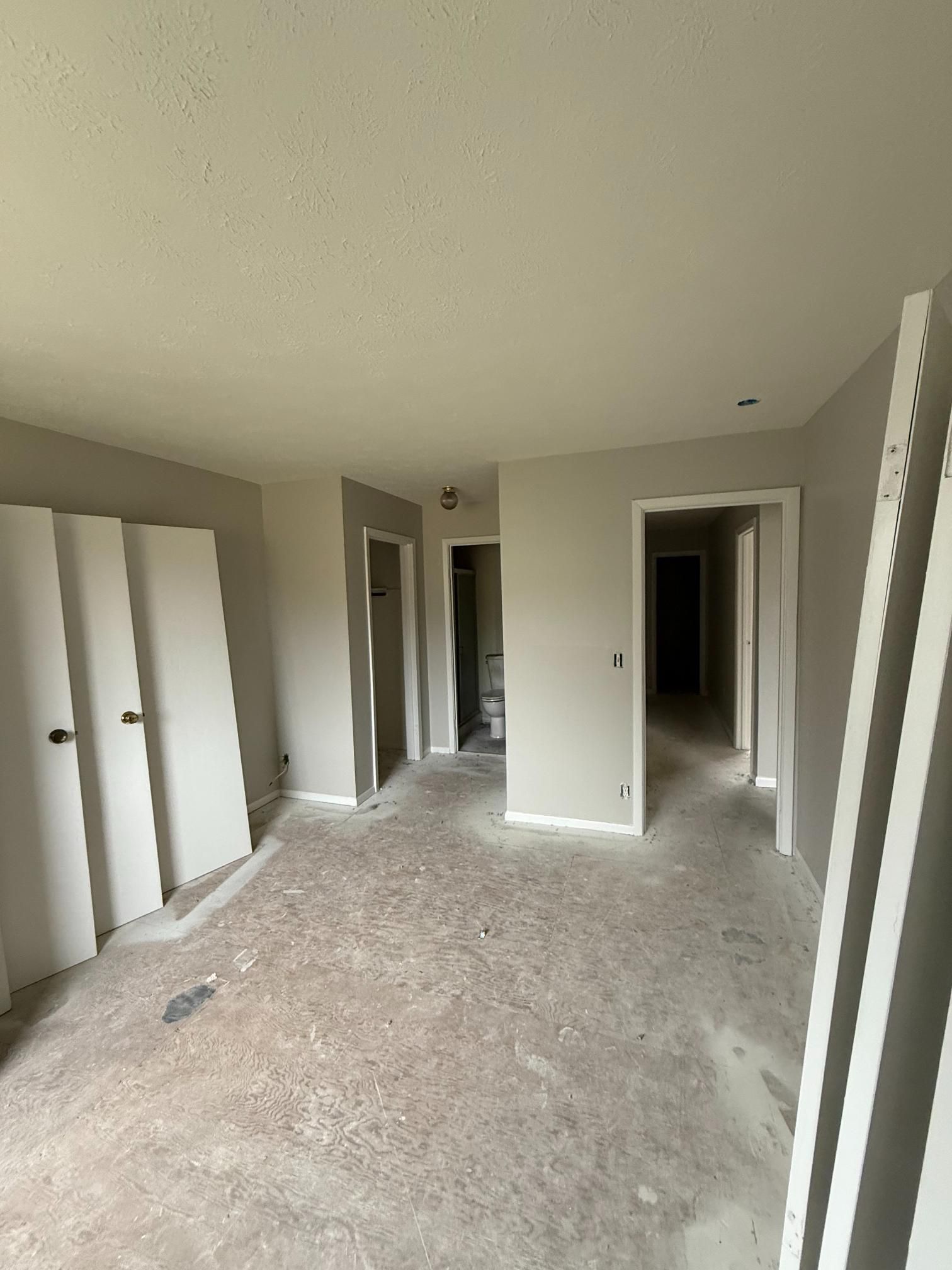 Empty room with gray walls, white doors, and concrete floor, possibly under construction.