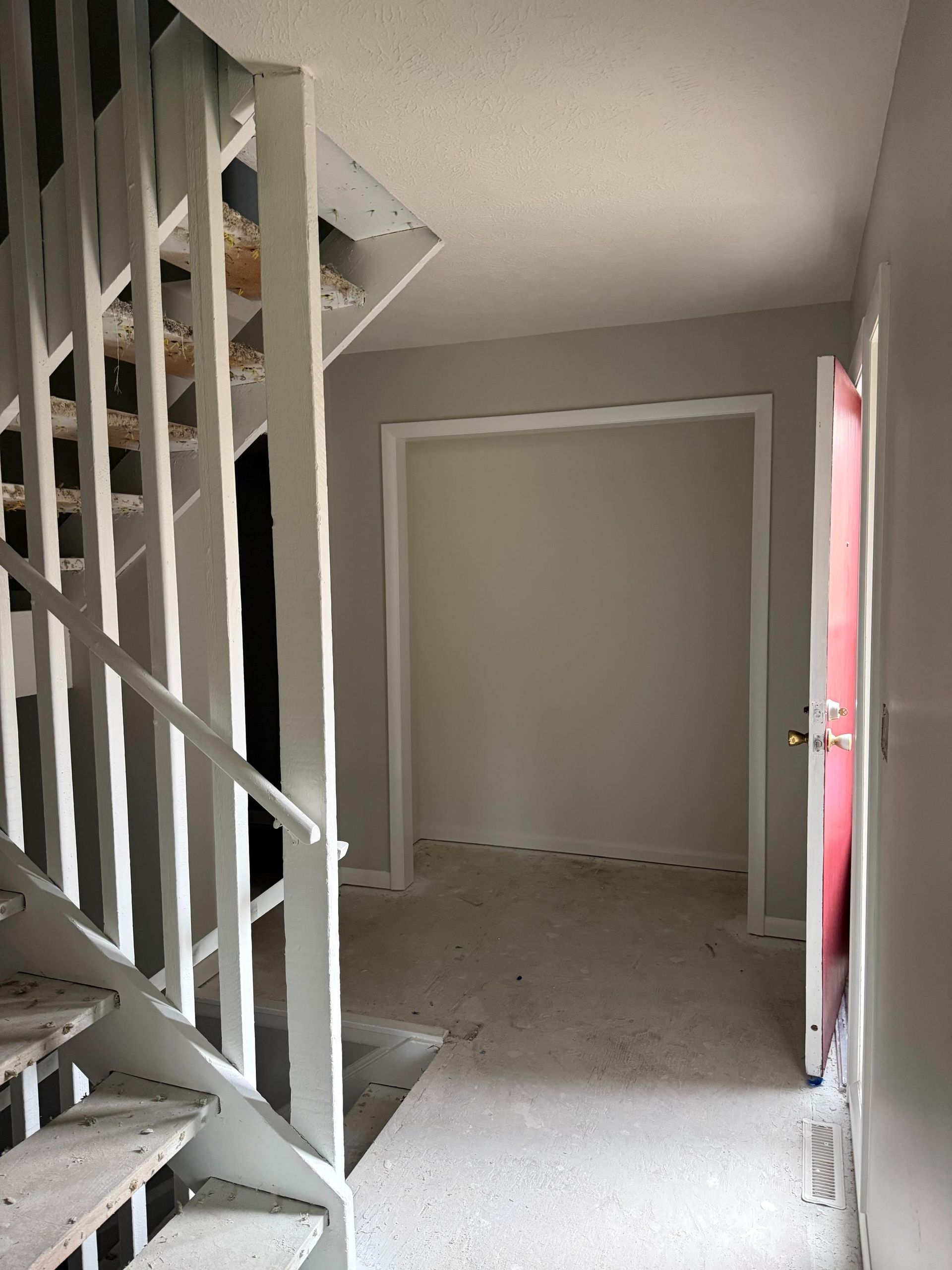 Interior hallway with stairs on the left, doorway straight ahead, and a door on the right, all painted in neutral tones.