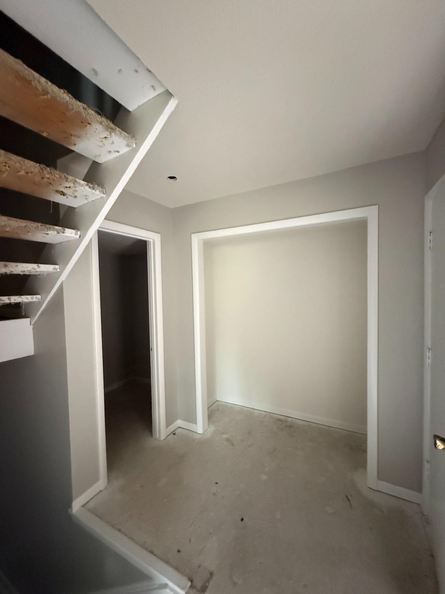 Interior view of a hallway with a staircase, closet, and doorways. Painted in shades of gray and white.