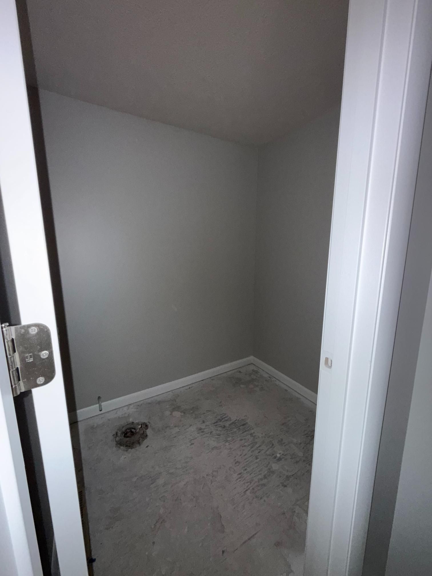 Small, gray-painted utility closet with a concrete floor. The open door frame is white.