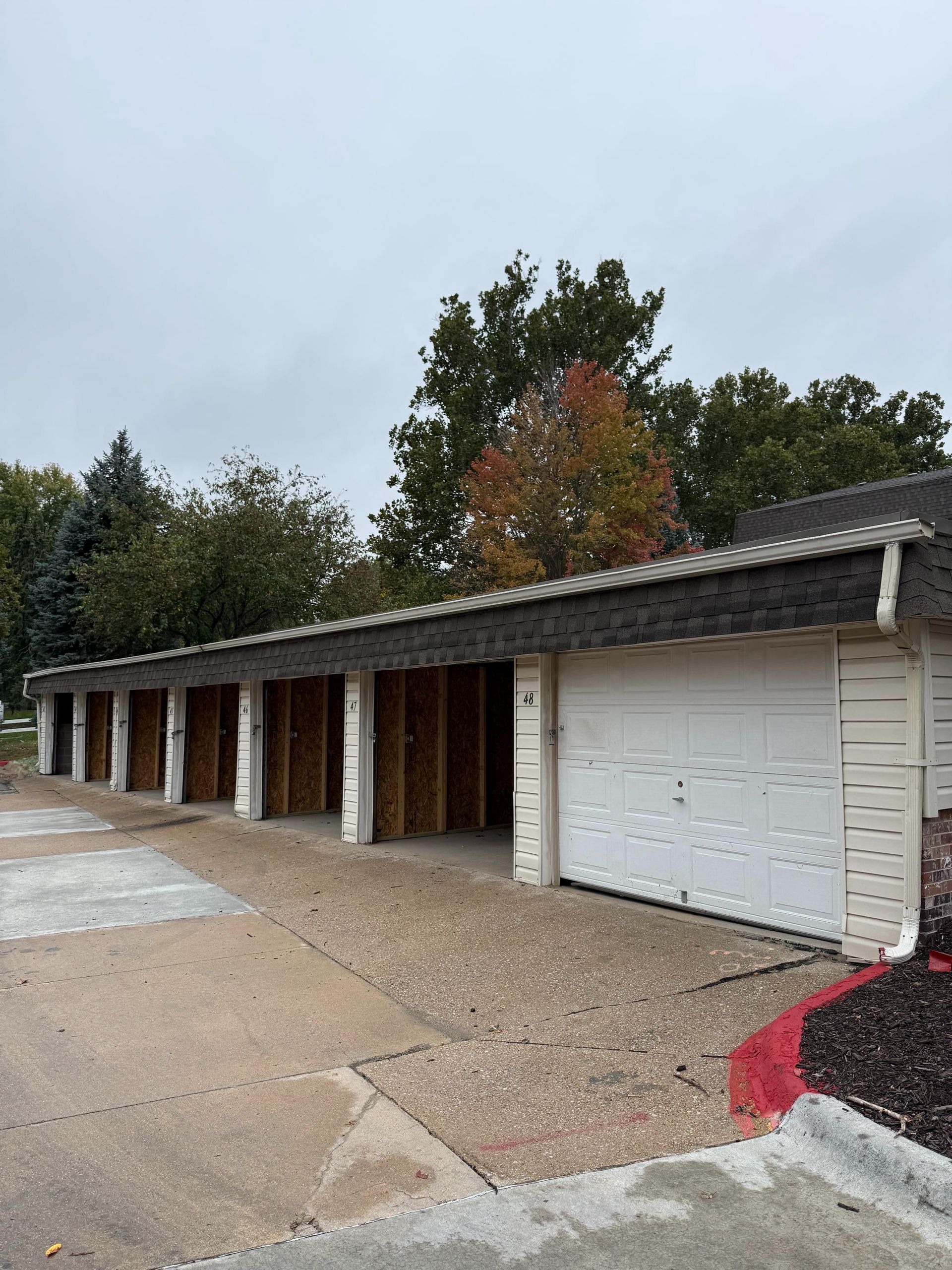 Row of garages, some with open frames, others with closed white doors, under a cloudy sky.