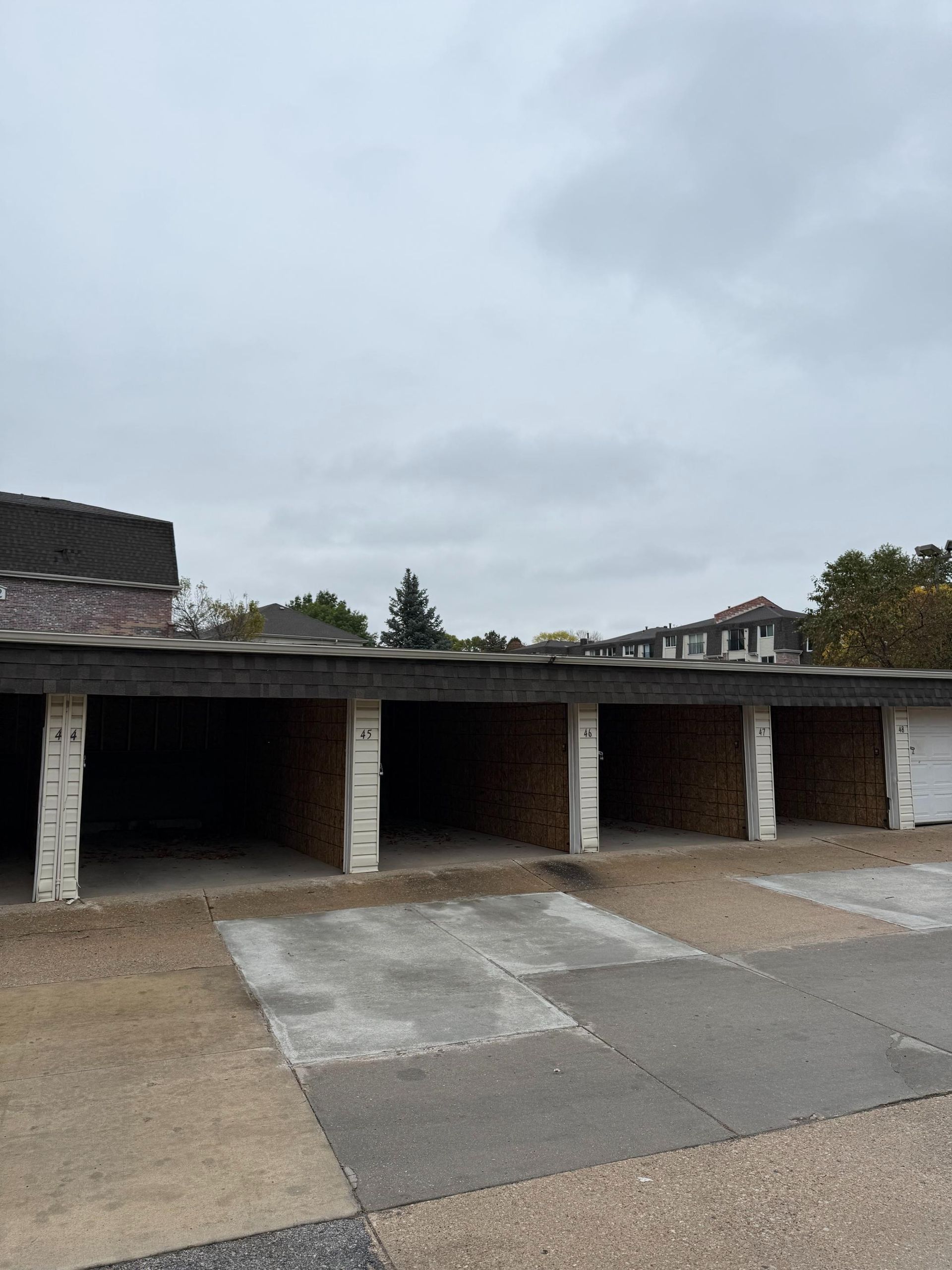Row of empty, open-front parking garages with cement floors under an overcast sky.