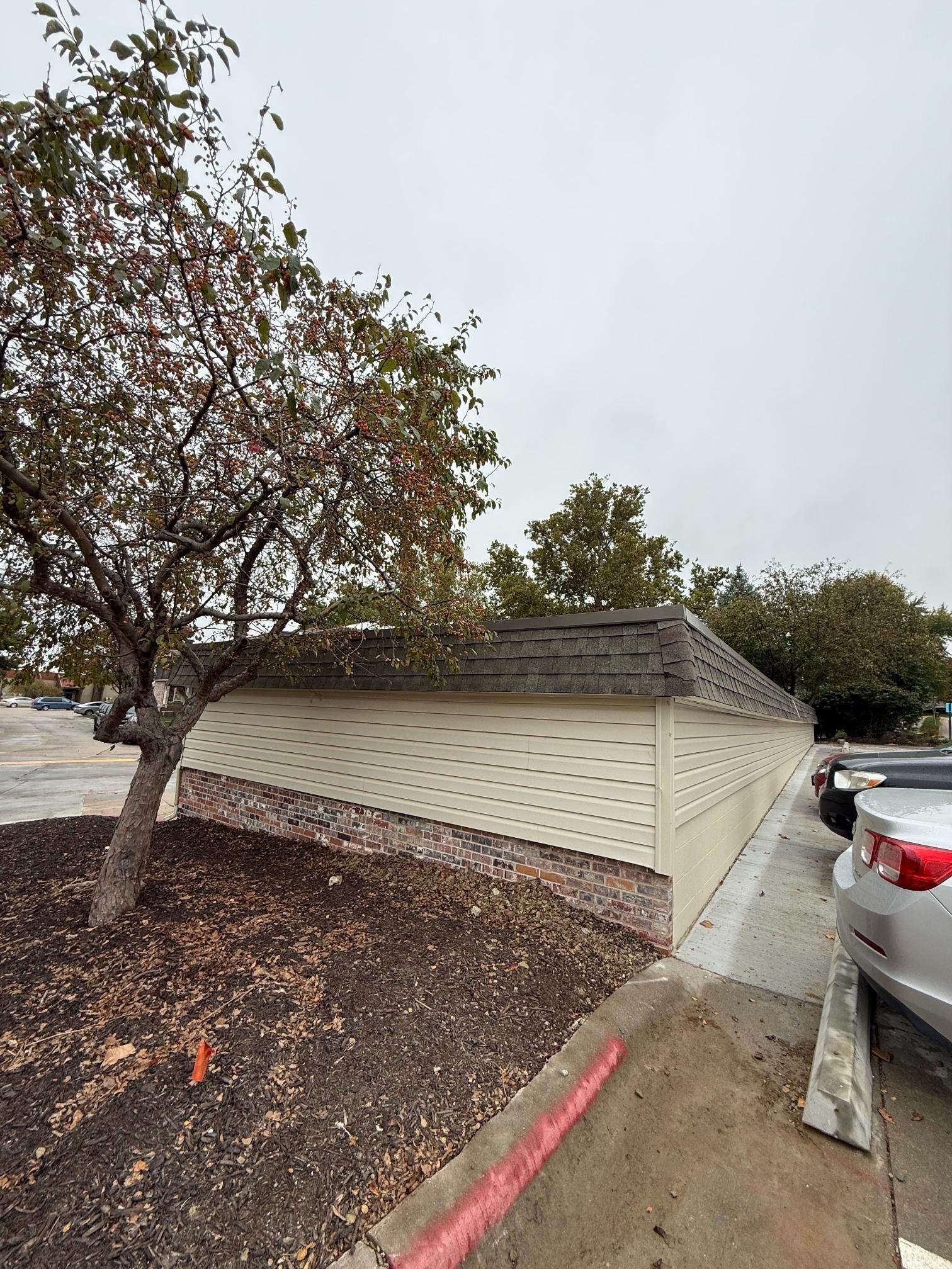 Beige building with a brown roof and a tree in front. A car is parked on the right.